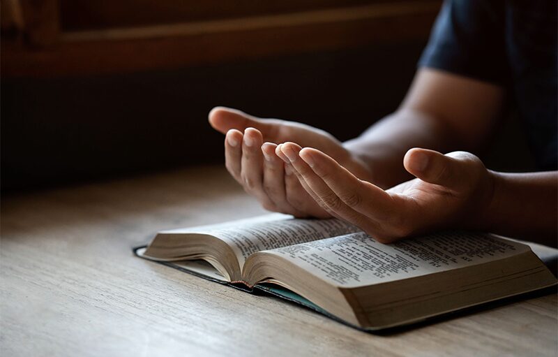 Open hands resting palm up beside an open Bible.